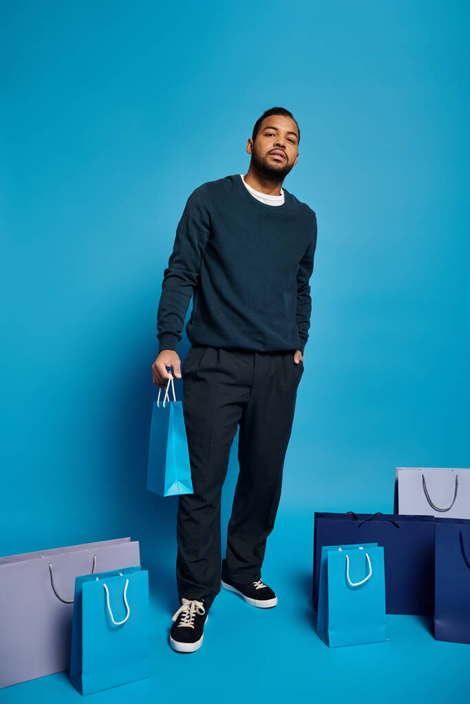 encantador homem americano africano em azul escuro roupa de pé com sacos de compras e mão no bolso - Foto, Imagem