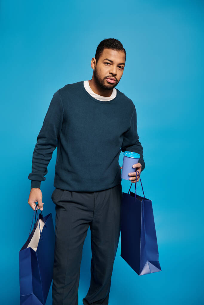 魅力的なアフリカ系アメリカ人男性が活気に満ちた背景に紙コップで買い物袋を持って - 写真・画像