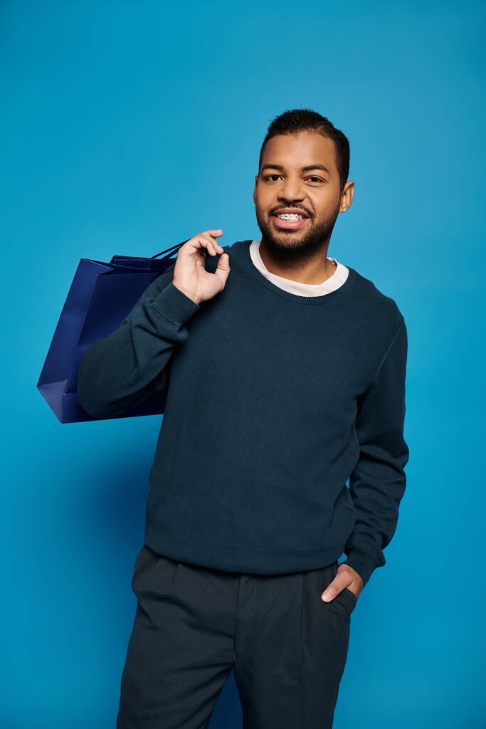 atractivo afroamericano joven con bolsa de compras sobre hombro y mano en bolsillo - Foto, Imagen