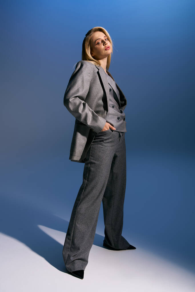 goed uitziende vrouw met blond haar in chique zilveren pak op zoek naar camera op donkerblauwe achtergrond - Foto, afbeelding