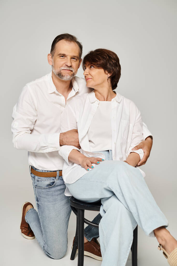 Retrato de pareja sonriente de mediana edad abrazando y mirando a la cámara sobre fondo gris - Foto, Imagen