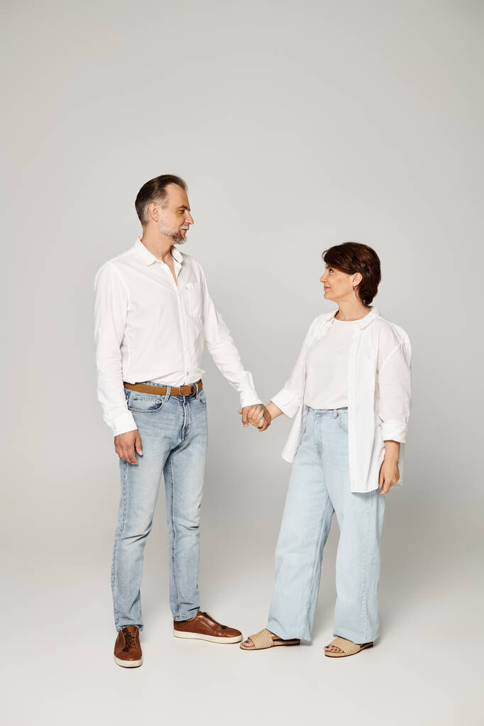 Plná délka záběr zralý krásný pár stojící na šedém pozadí a při pohledu na sebe - Fotografie, Obrázek