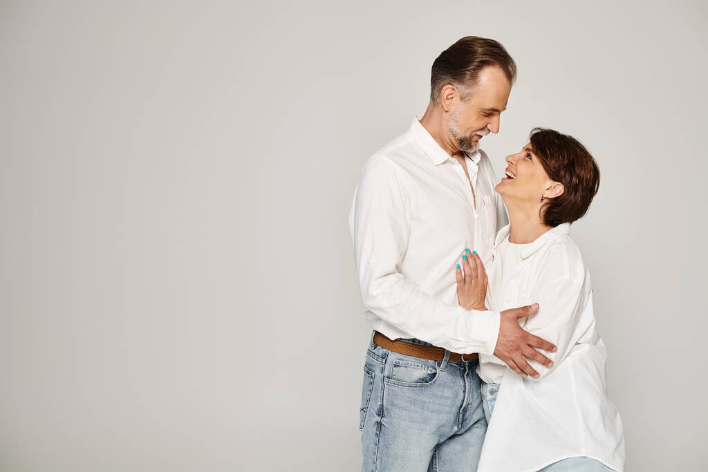 Ritratto di coppia sorridente di mezza età che si abbraccia e si guarda su sfondo grigio - Foto, immagini