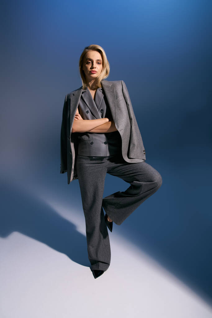 стильная женщина в серебристом элегантном жилете и костюме позирует на темно-синем фоне и смотрит в камеру - Фото, изображение