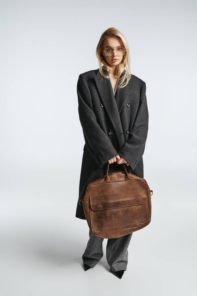 Güzel, modaya uygun, gözlüklü, kahverengi çantalı, siyah zarif ceketli bir kadın kameraya bakıyor. - Fotoğraf, Görsel