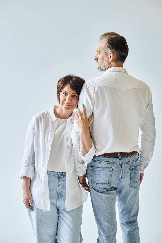Приваблива жінка середнього віку обіймає зрілого чоловіка рукою з любов'ю на сірому фоні - Фото, зображення