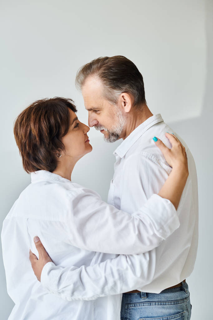Gri arka planda sarılıp öpüşen orta yaşlı bir çiftin yan görünüm portresi - Fotoğraf, Görsel
