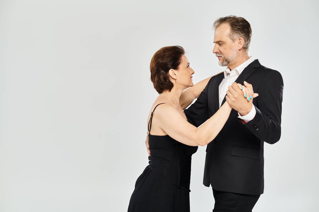 Portret atrakcyjnej pary w średnim wieku w tango dance pozie odizolowanej na szarym tle - Zdjęcie, obraz