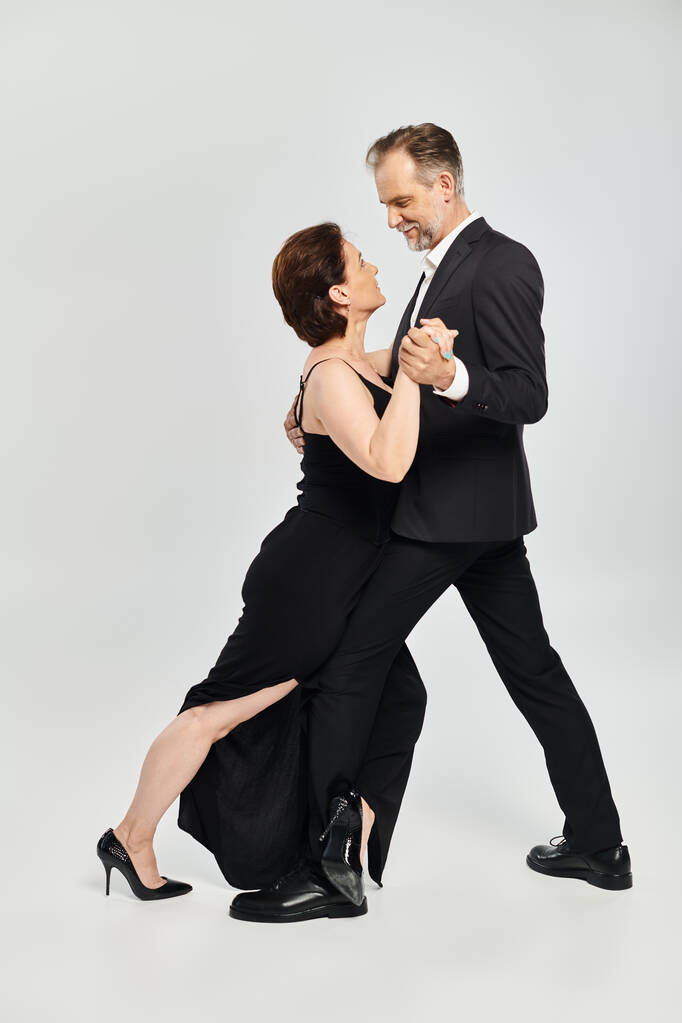 Baile de salón pareja de mediana edad en una pose de baile y sonriente aislado sobre fondo gris - Foto, imagen
