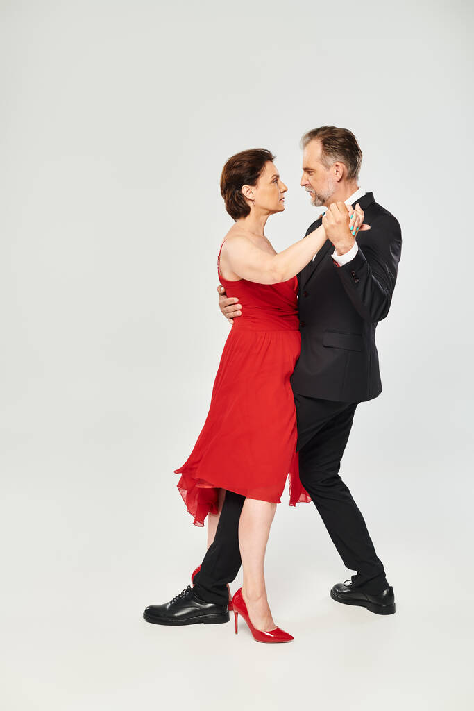 Teljes hosszúságú kép érett vonzó pár piros ruha és öltöny tánc szürke háttér - Fotó, kép