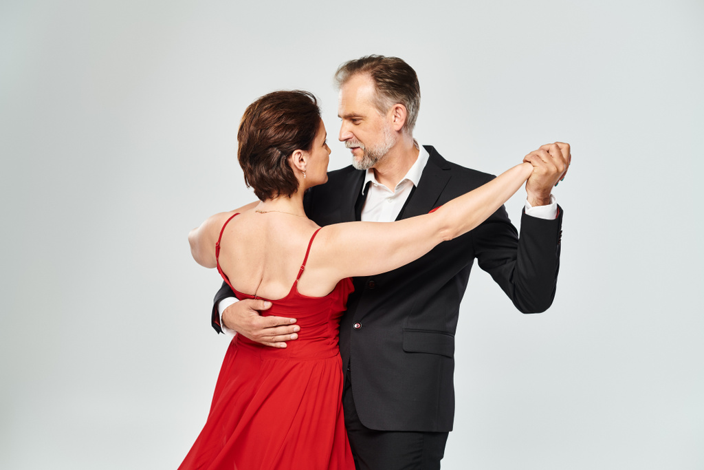 Mature attractive smiling couple dancing ballroom dance isolated on grey background - Photo, Image
