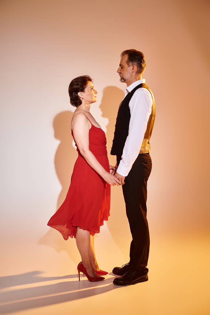Attraente coppia di ballerini sorridenti di mezza età in abito rosso e vestito con luce gialla sul grigio - Foto, immagini