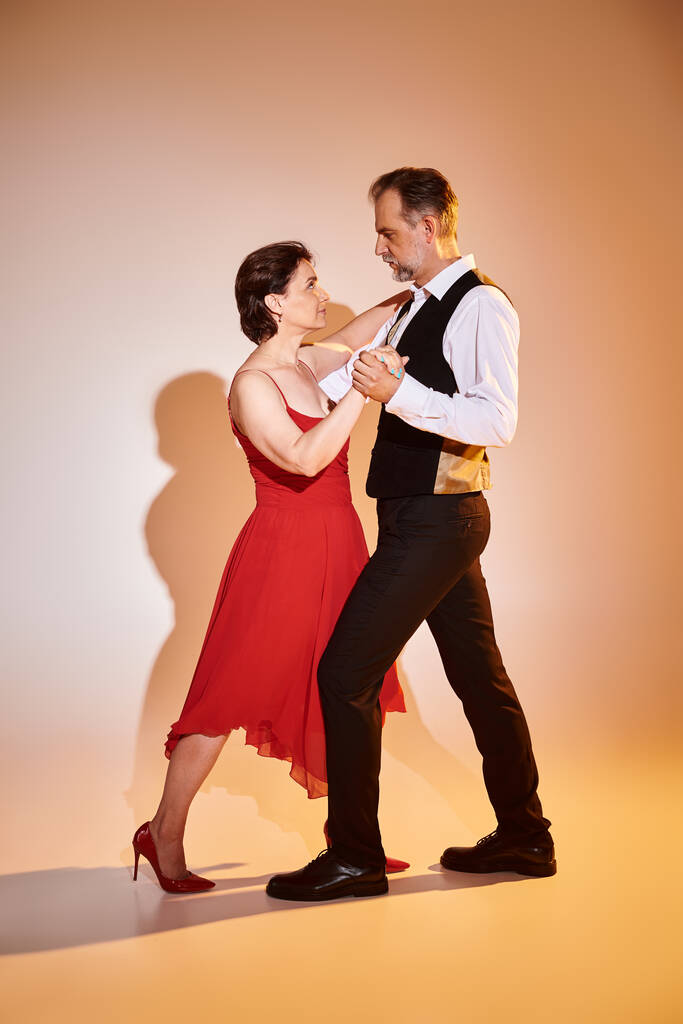 Ballroom dance middle aged couple in red dress and suit dancing tango with yellow light on grey - Photo, Image