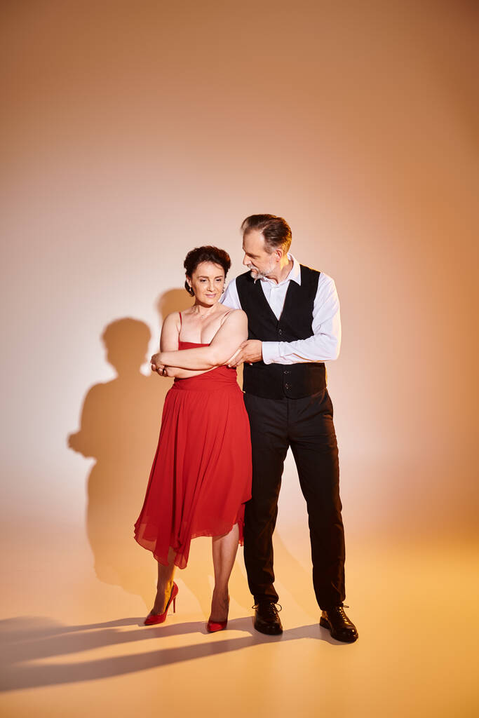 Danseurs couple souriants attrayants d'âge moyen en robe rouge et costume avec lumière jaune sur gris - Photo, image