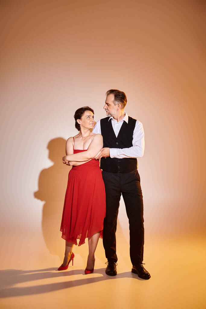 Retrato de pareja atractiva de mediana edad en vestido rojo y traje de pie sobre fondo gris - Foto, imagen