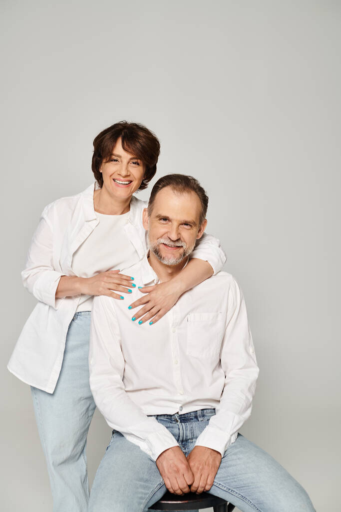 Портрет мужчины и женщины средних лет, смотрящих в камеру и улыбающихся на сером фоне - Фото, изображение