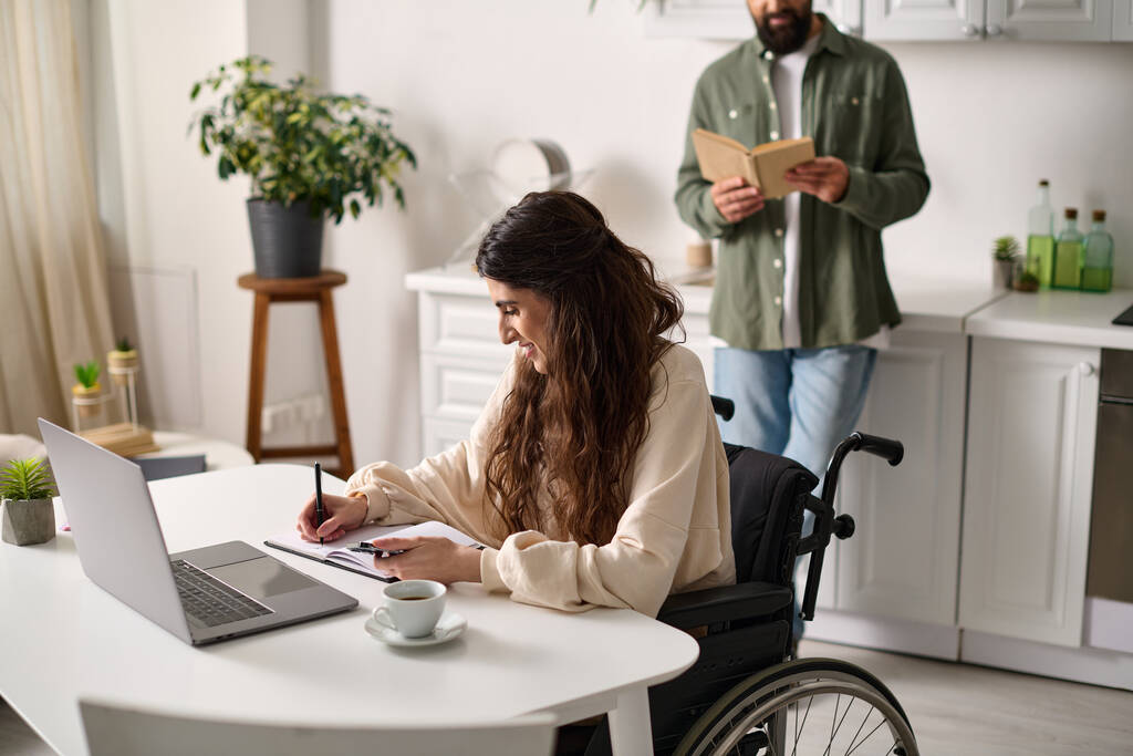 femme joyeuse avec un handicap de mobilité travaillant de la maison à côté de son livre de lecture hasband barbu - Photo, image