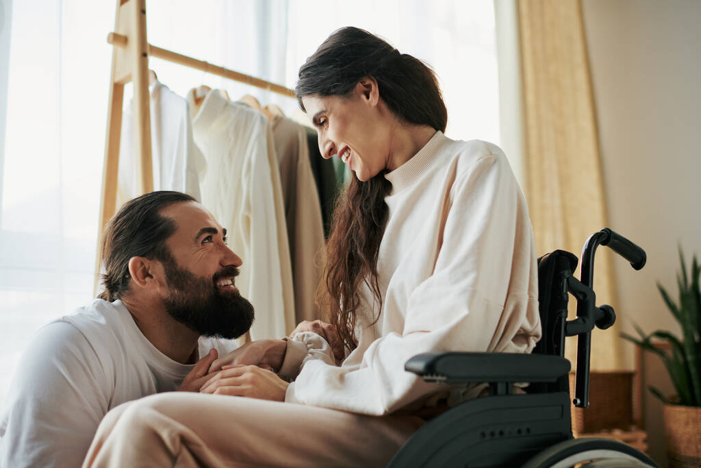 привабливий веселий чоловік проводить час зі своєю красивою дружиною-інвалідом, перебуваючи в спальні вдома - Фото, зображення