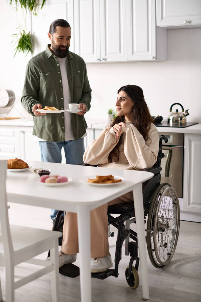 бородатый любящий мужчина приносит свою весёлую жену с тостами для инвалидов и горячим кофе за завтраком - Фото, изображение