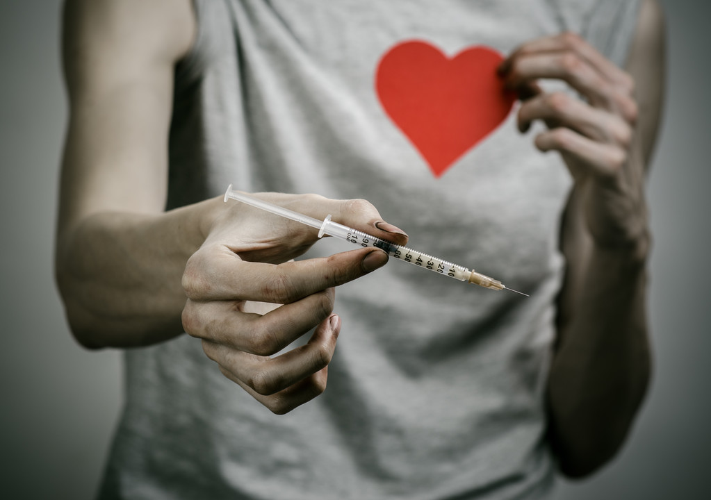 A luta contra as drogas e toxicodependência tópico: viciado sujo magro segurando uma seringa com uma droga e coração vermelho em um fundo escuro
 - Foto, Imagem