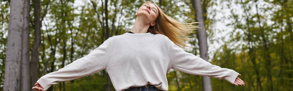 Спокійна і розслаблена блондинка танцює в лісових джинсах і светрі під час поїздки на рюкзаку, банер - Фото, зображення