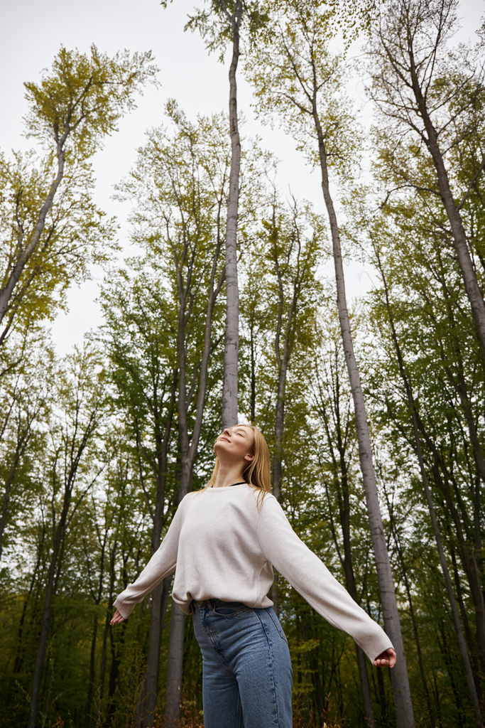 Meditar chica rubia en acogedor, suéter senderismo en el bosque y tener un momento tranquilo con los ojos cerrados - Foto, Imagen