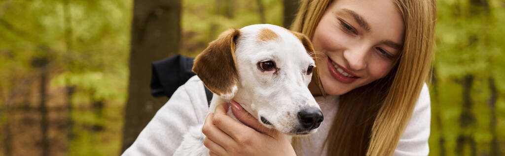 笑顔の金髪の女性は彼女の犬を抱擁し,森林旅行中に停止している間,彼女のペットの世話,バナー - 写真・画像