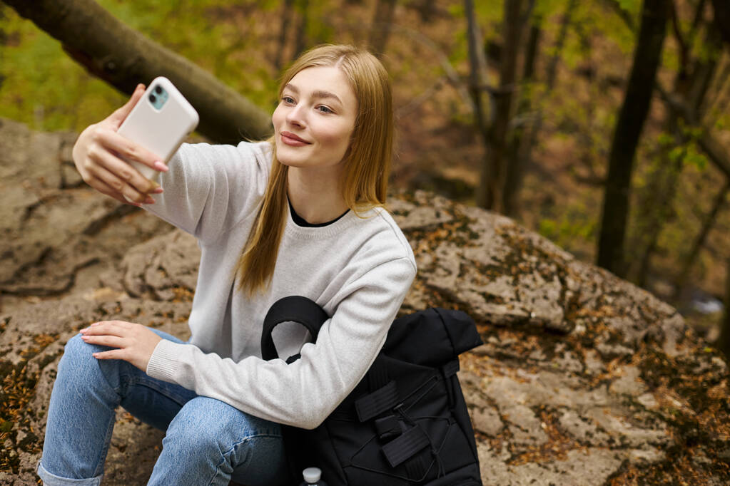Χαμογελώντας ειρηνική ξανθιά νεαρή γυναίκα λήψη selfie, ενώ χαλαρώνοντας στο δάσος, ενώ πεζοπορία - Φωτογραφία, εικόνα