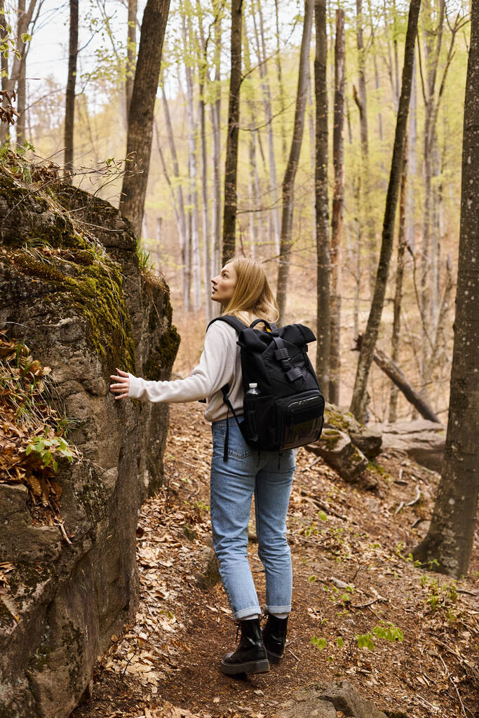 Visszapillantás kíváncsi szőke nő visel hátizsák túrázás és séta közelében sziklás szikla - Fotó, kép