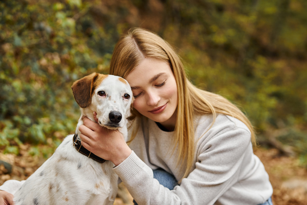 Gülümseyen kadın orman gezisinde köpek arkadaşına nazikçe sarılıyor. - Fotoğraf, Görsel