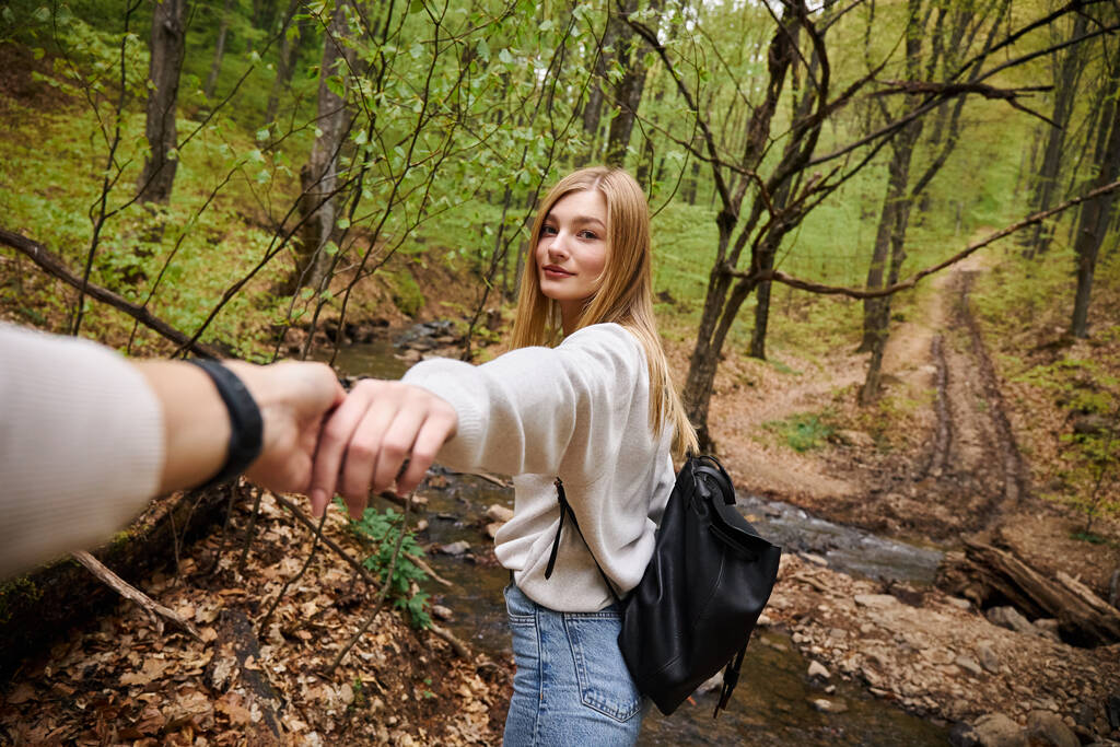Mujer joven liderando camino, punto de vista foto de pareja cogida de la mano cruzando el arroyo en el bosque - Foto, imagen