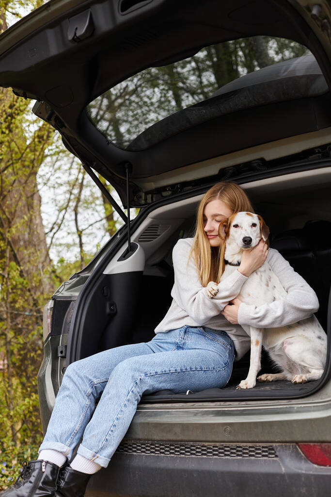 笑顔の幸せな女性は,ハイキング旅行中,森の中で車の後ろに座っている彼女の犬を抱きしめます - 写真・画像