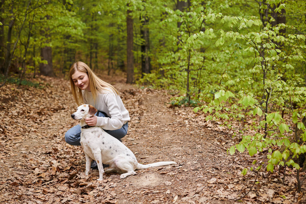 Gülümseyen yürüyüşçü kız hayvanıyla etkileşime giriyor. Orman manzaralı yürüyüş yaparken yöne bakıyor. - Fotoğraf, Görsel