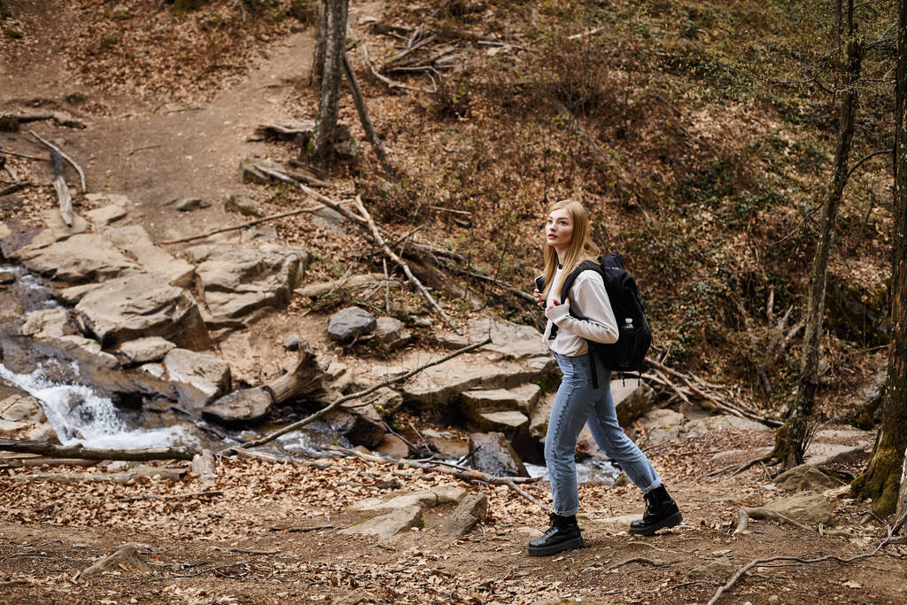 Young female hiker crossing the forest creek, having backpack trip near in the woods - Photo, Image