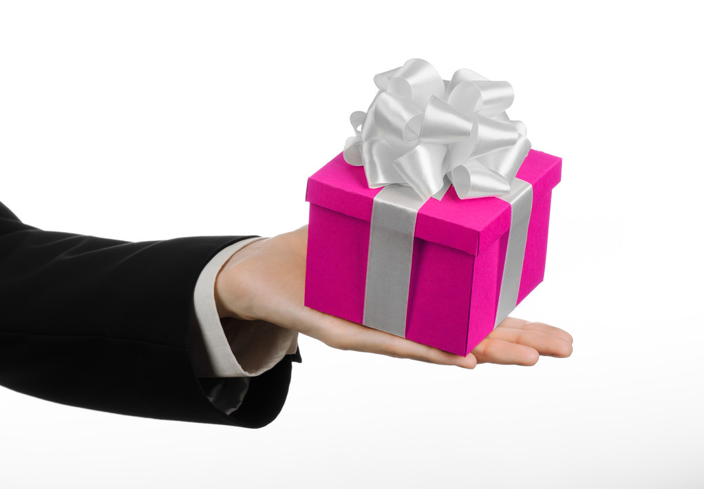 Le thème des célébrations et des cadeaux : main tenant un cadeau enveloppé dans une boîte rose avec ruban blanc et arc, le plus beau cadeau isolé sur fond blanc en studio
 - Photo, image