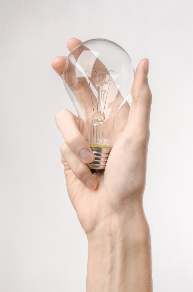 Тема енергоспоживання та енергозбереження: рука людини тримає лампочку на білому тлі в студії
 - Фото, зображення