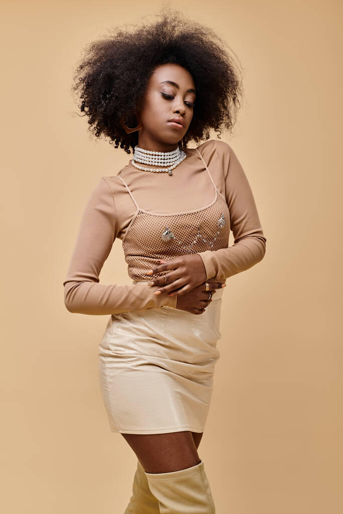 young african american woman with curly hair posing in stylish pastel outfit on a beige backdrop - Photo, Image