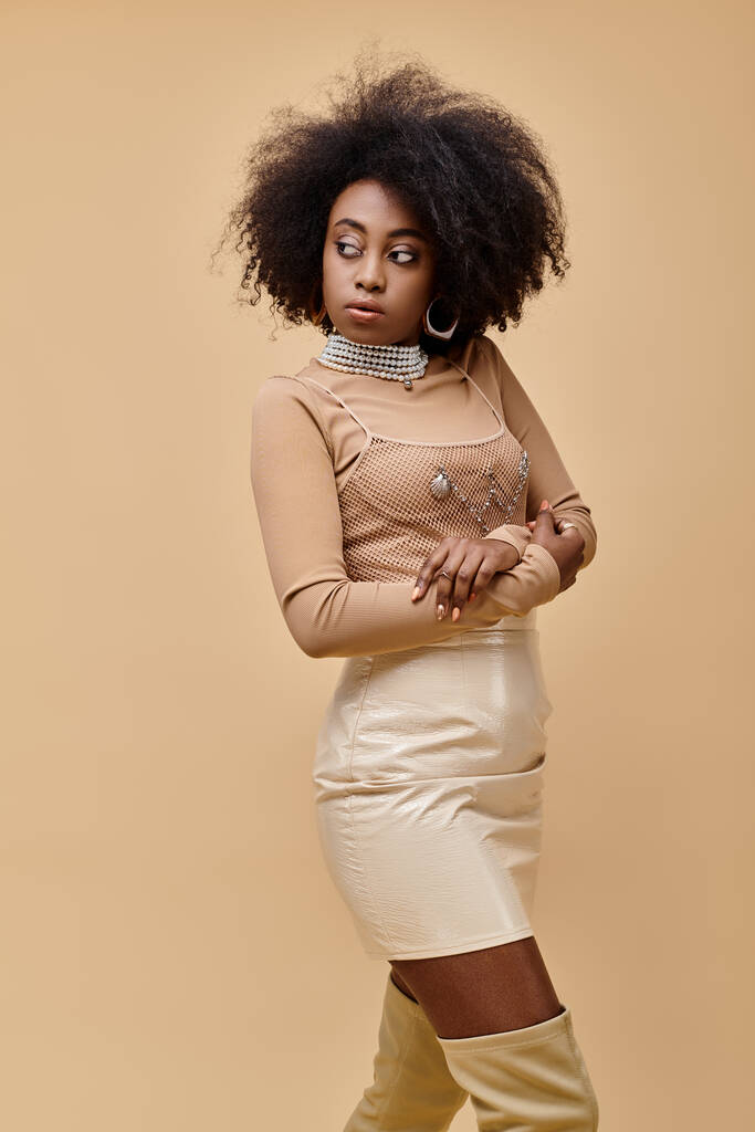 young african american woman with curly hair posing in pastel peach outfit on beige backdrop - Photo, Image