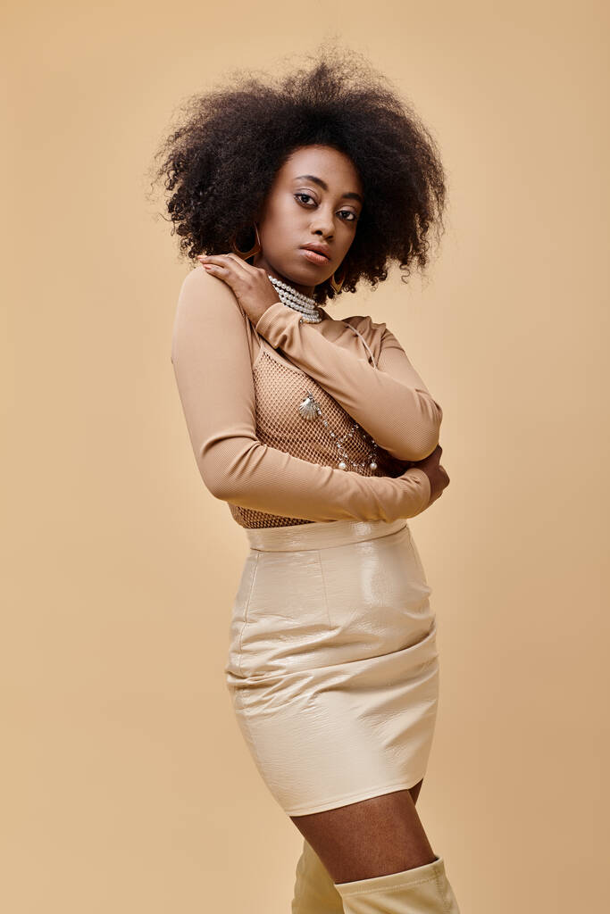 jovem modelo afro-americano com cabelo encaracolado posando em roupa de pêssego pastel em pano de fundo bege - Foto, Imagem