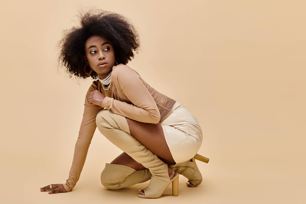 młody Afryki amerykański model w stylowy pastelowy strój i nogi wysokie buty pozowanie na beżowy - Zdjęcie, obraz