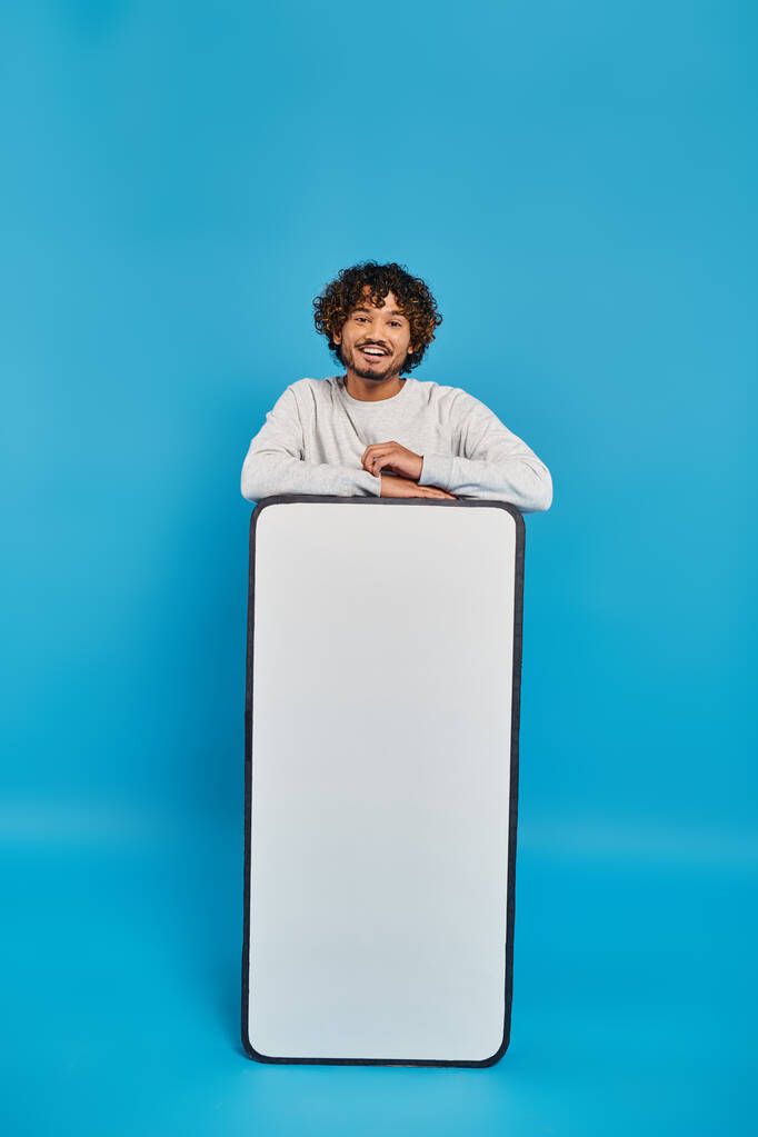 Ein Mann steht versteckt hinter einem großen weißen Objekt in einem Studio auf blauem Hintergrund. - Foto, Bild
