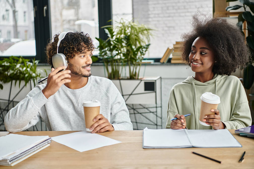 Ein Mann und eine Frau unterschiedlicher Kulturen sitzen an einem Tisch, schlürfen Kaffee und unterhalten sich in einem modernen Coworking Space. - Foto, Bild