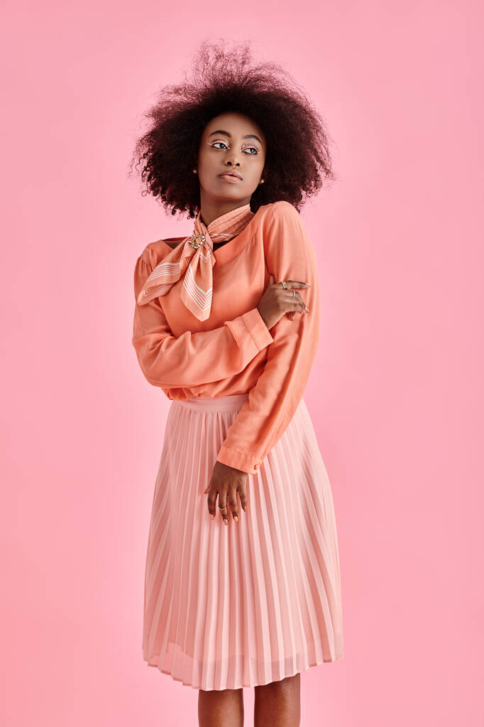 ricci donna africana americana in camicetta color pesca, gonna midi e sciarpa collo in posa su sfondo rosa - Foto, immagini