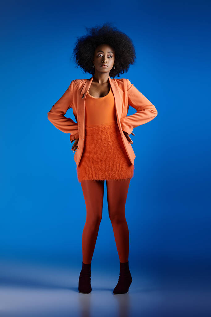 fiatal afro-amerikai nő texturált ruha és blézer pózol magas sarkú, élénk kék háttér - Fotó, kép