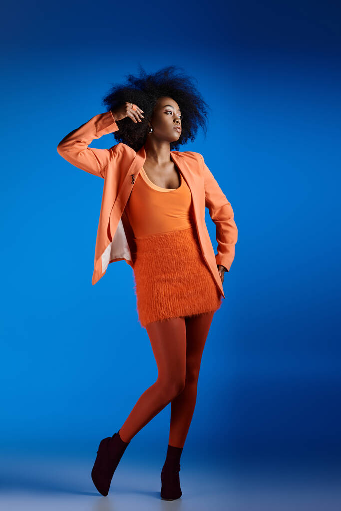 σγουρά νεαρά αφροαμερικανικά μοντέλο σε υφή φόρεμα και σακάκι ποζάρουν με το χέρι στο ισχίο σε μπλε - Φωτογραφία, εικόνα