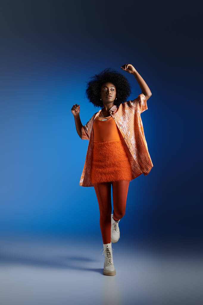look tendance du modèle afro-américain en chemise à motifs et robe texturée posant sur fond bleu - Photo, image