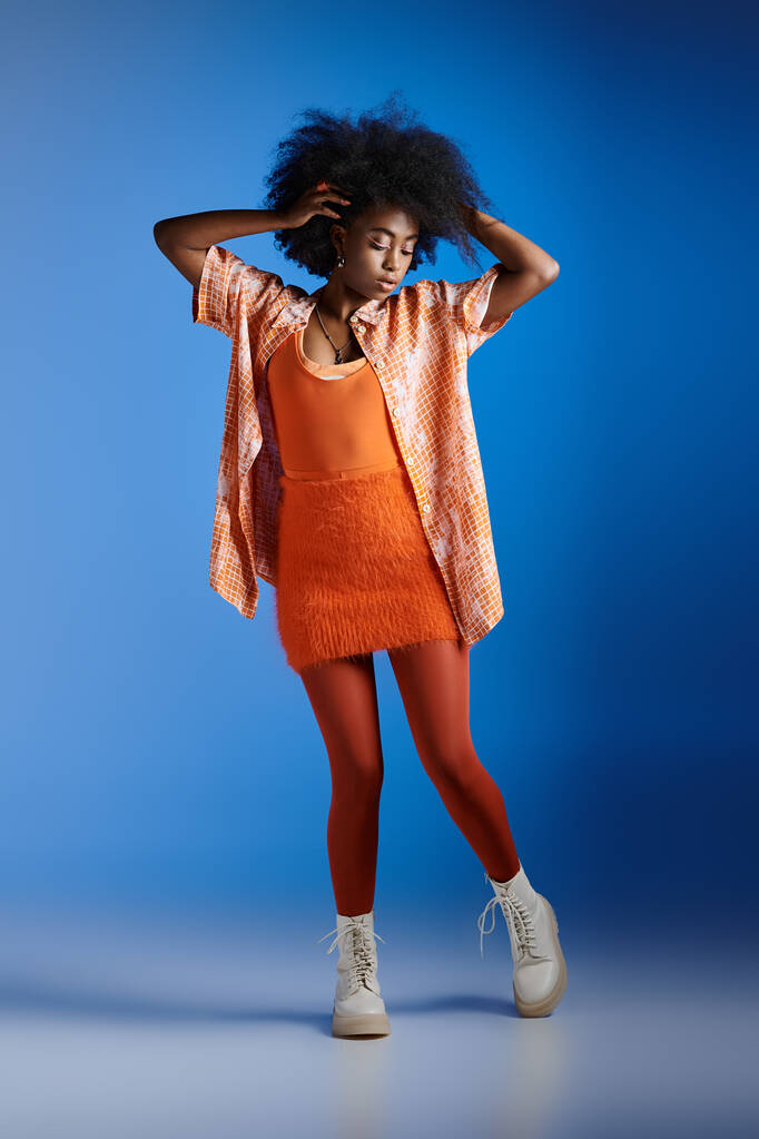модная африканская модель в узорчатой рубашке и модном платье, позирующем на синем фоне - Фото, изображение