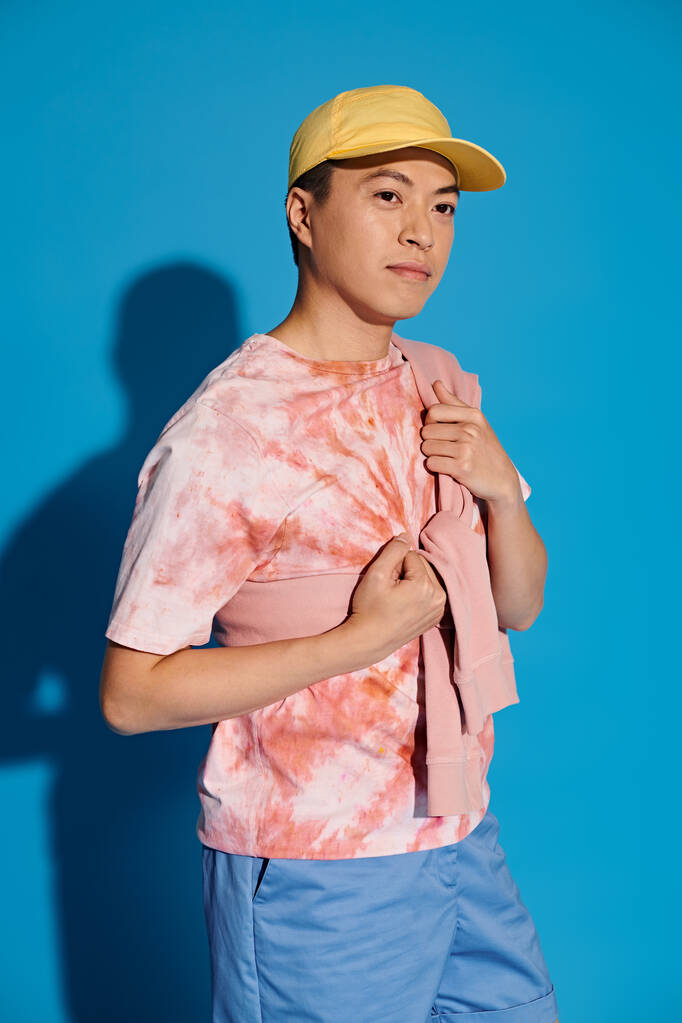 A stylish young man in a tie-dyed shirt poses actively on a blue backdrop. - Photo, Image