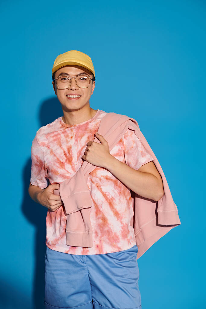 Stijlvolle jongeman die energiek poseert in een trendy roze shirt en blauwe short tegen een levendige blauwe achtergrond. - Foto, afbeelding