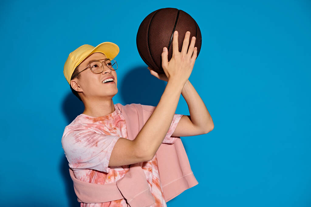 Een stijlvolle vrouw met een gele hoed houdt vol vertrouwen een basketbal, straalt energie en kracht uit tegen een levendige achtergrond. - Foto, afbeelding